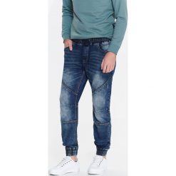SPODNIE MĘSKIE TYPU JOGGER Z DZIANINY IMITUJĄCEJ JEANS. Niebieskie joggery i bojówki TOP SECRET, l, bez wzorów, z dzianiny. W wyprzedaży za 64.99 zł.