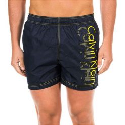 Szorty kąpielowe w kolorze granatowo-żółtym. Klapki marki CALVIN KLEIN. W wyprzedaży za 195.95 zł.