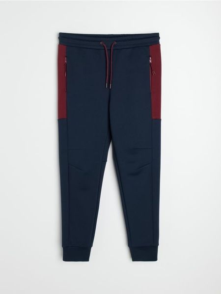 Sportowe spodnie jogger z kontrastowymi panelami i kieszeniami na zamek - granatowy. Niebieskie joggery i bojówki Sinsay, l, bez wzorów, sportowe. Za 69.99 zł.