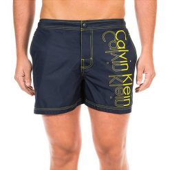 Szorty kąpielowe w kolorze granatowo-żółtym. Klapki marki CALVIN KLEIN. W wyprzedaży za 195.95 zł.